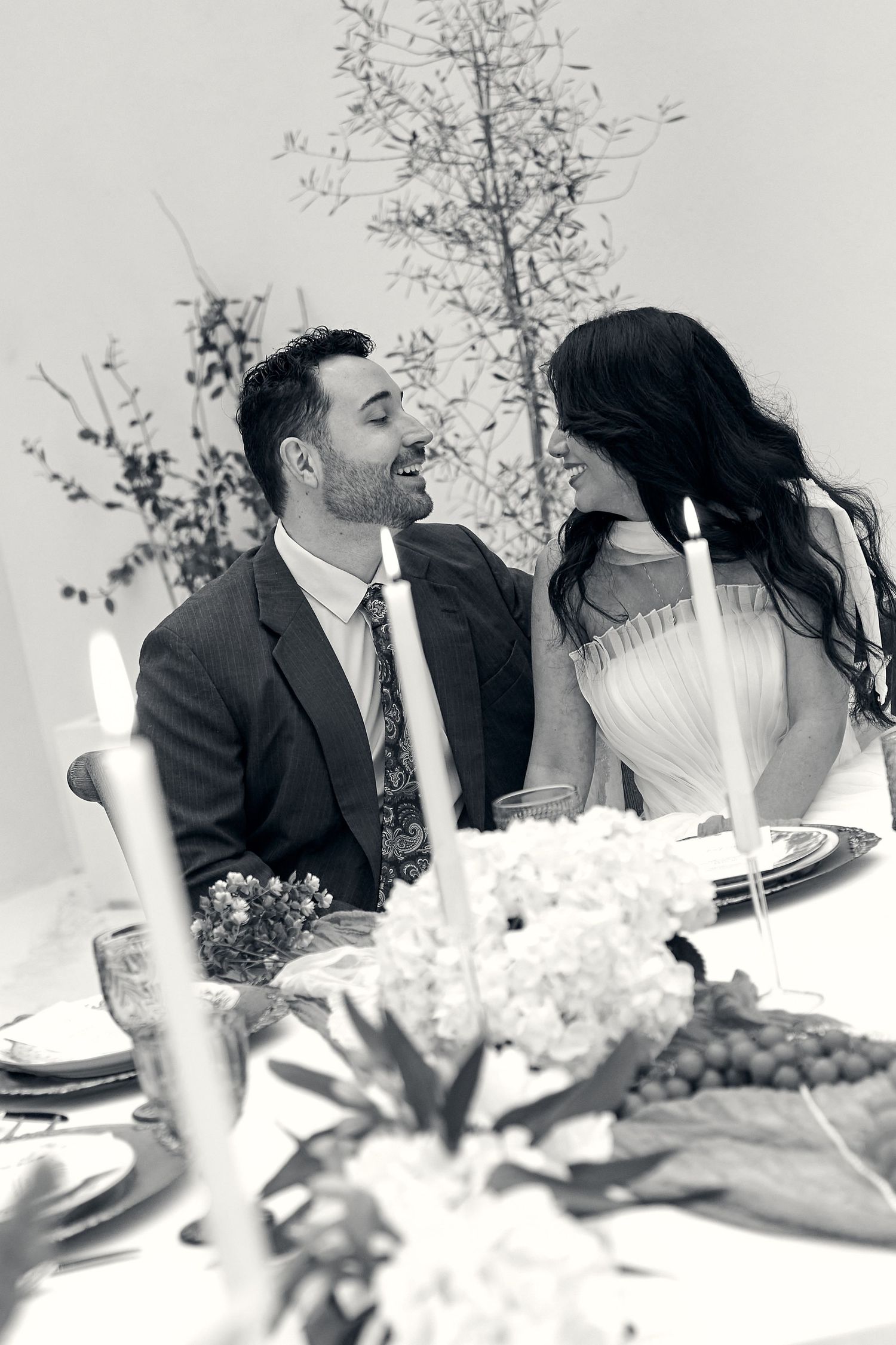 A black and white photo of a couple at their wedding reception table with candles and floral decor.