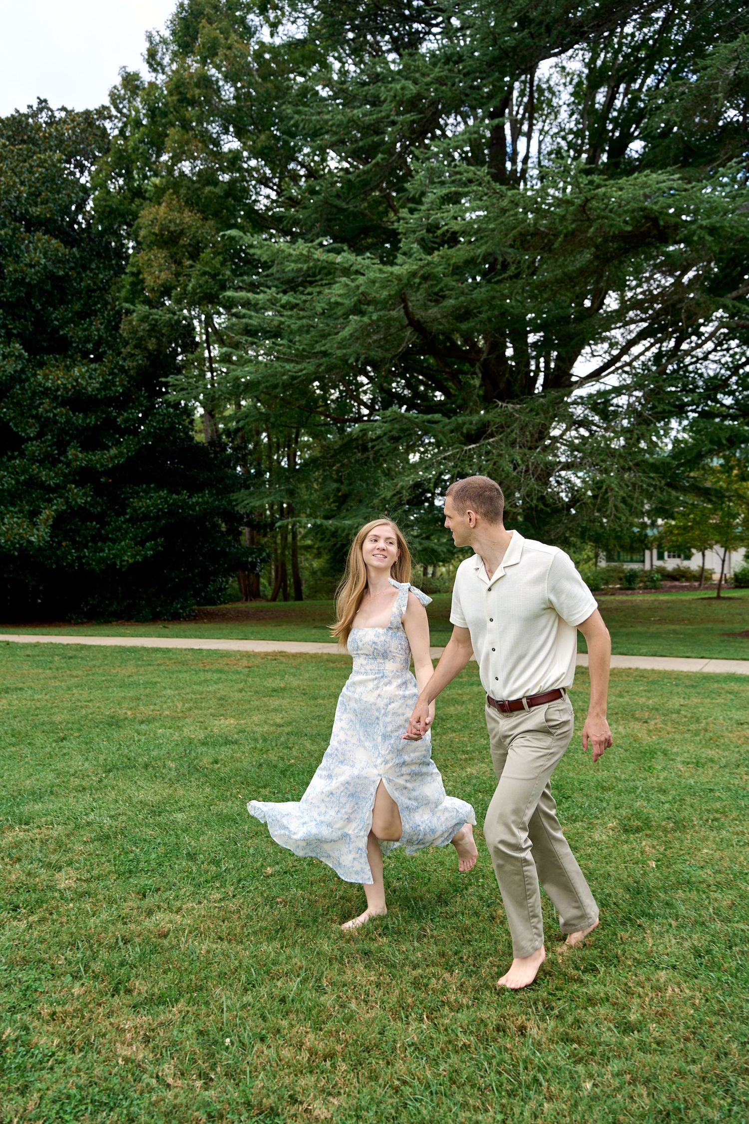Happy couple holding hands and running barefoot across a green park lawn.