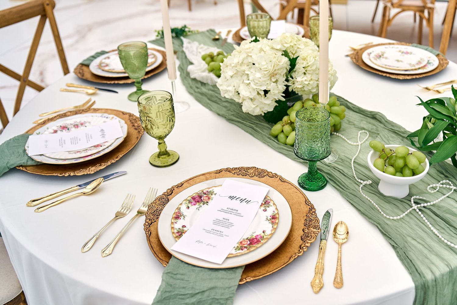 Elegant table setting with gold chargers, green glassware, sage runner and white hydrangea centerpiece.