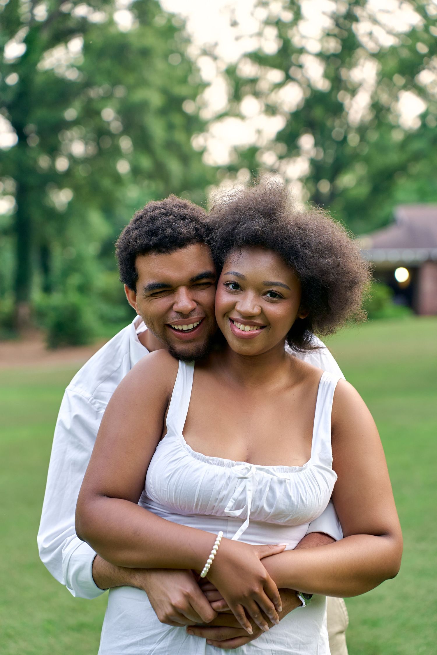 A happy couple embraces and smiles while sharing a tender moment in a park setting.
