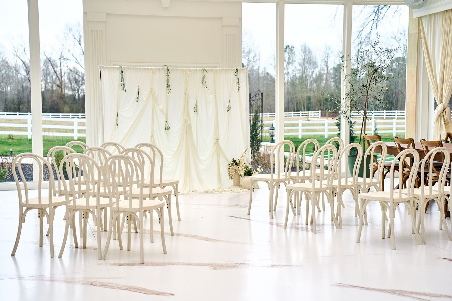 Light and airy indoor wedding ceremony setup with bentwood chairs and white drapery in a bright sunlit room.