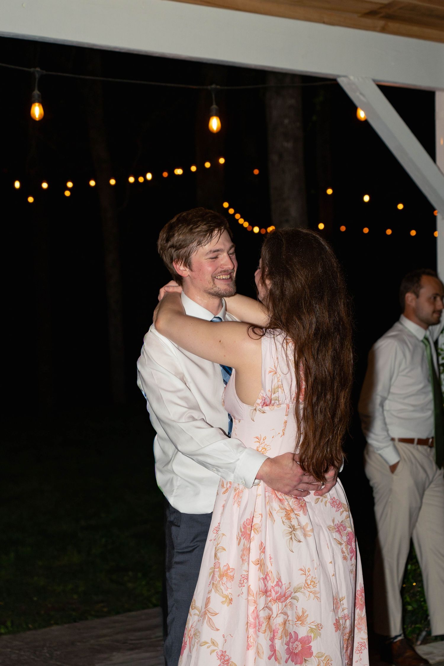 Couple slow dancing outdoors at night under string lights at a wedding reception.