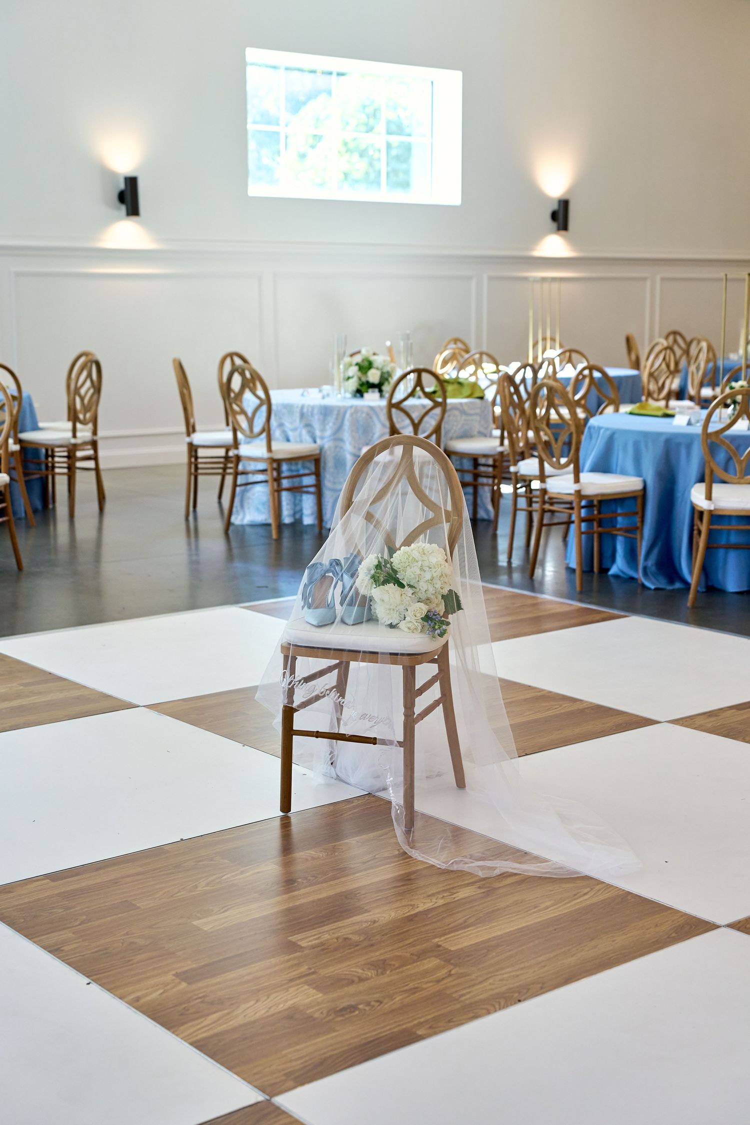 Wedding reception hall with checkered dance floor, gold chairs, and blue table linens.