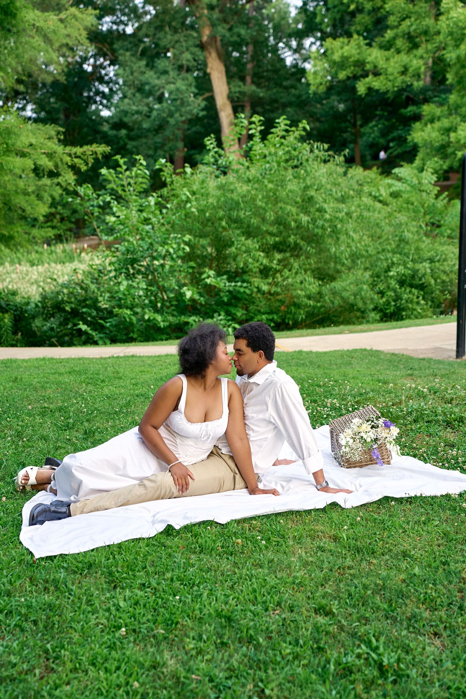 A tender moment shared between a couple laying on a white blanket in a lush green park.