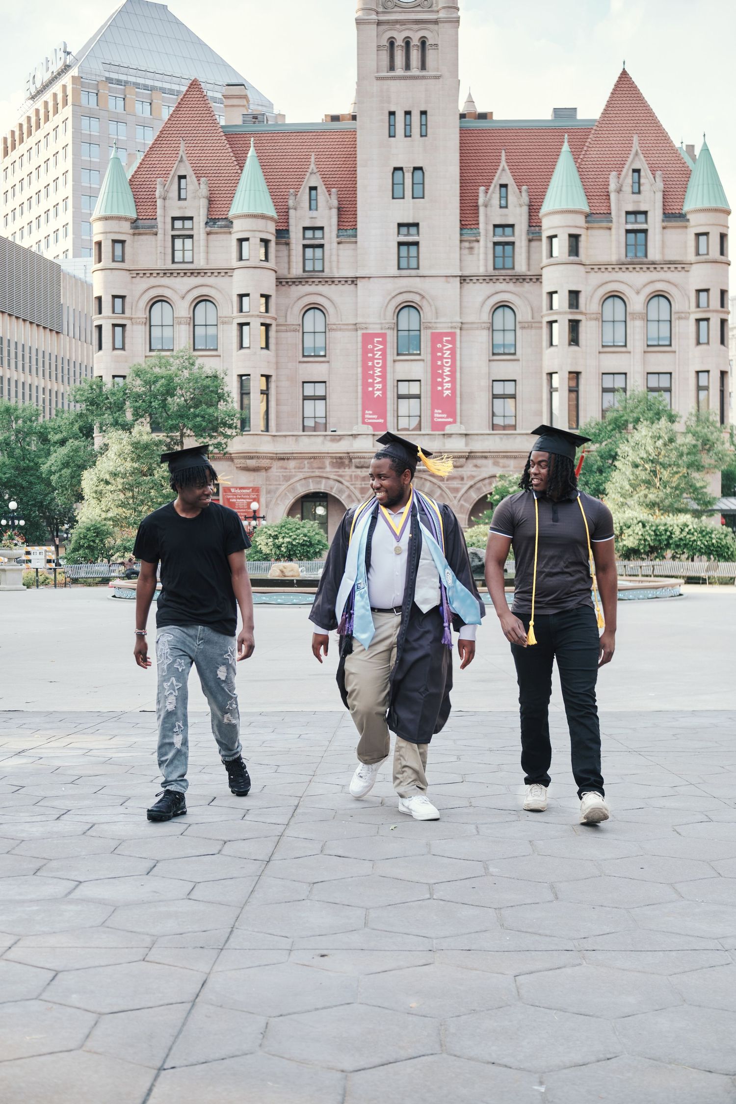 Three graduates in caps celebrating outdoors in front of historic university building.