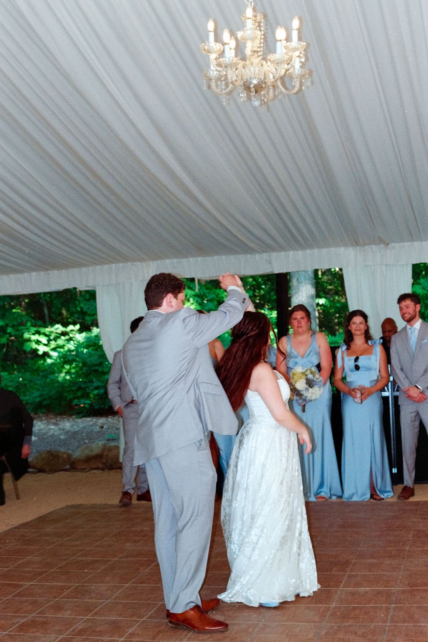 Bride and groom share first dance under chandelier in elegant white draped tent.