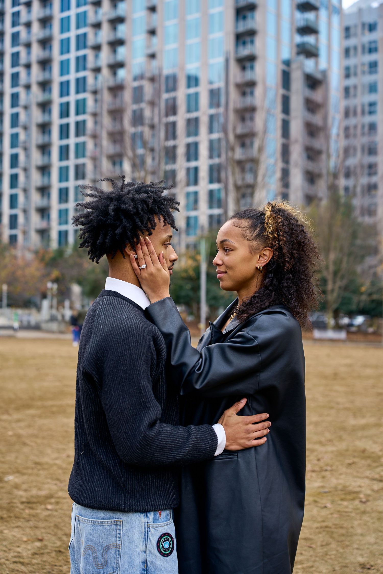 Two people in dark outfits share intimate moment while standing in front of urban apartment buildings. North Carolina Wedding Photographer.