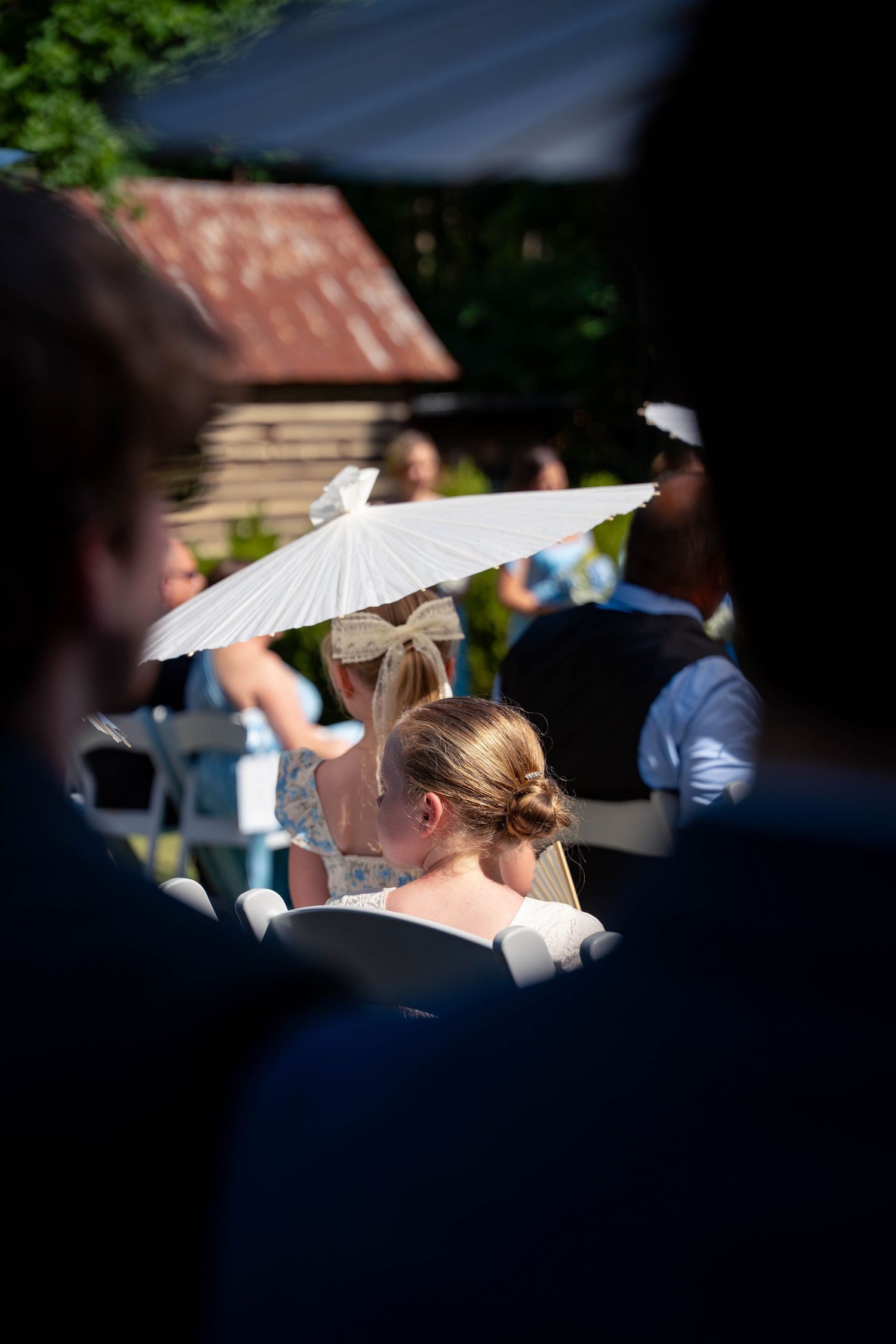 Guest holding white parasol at outdoor wedding ceremony on sunny day.