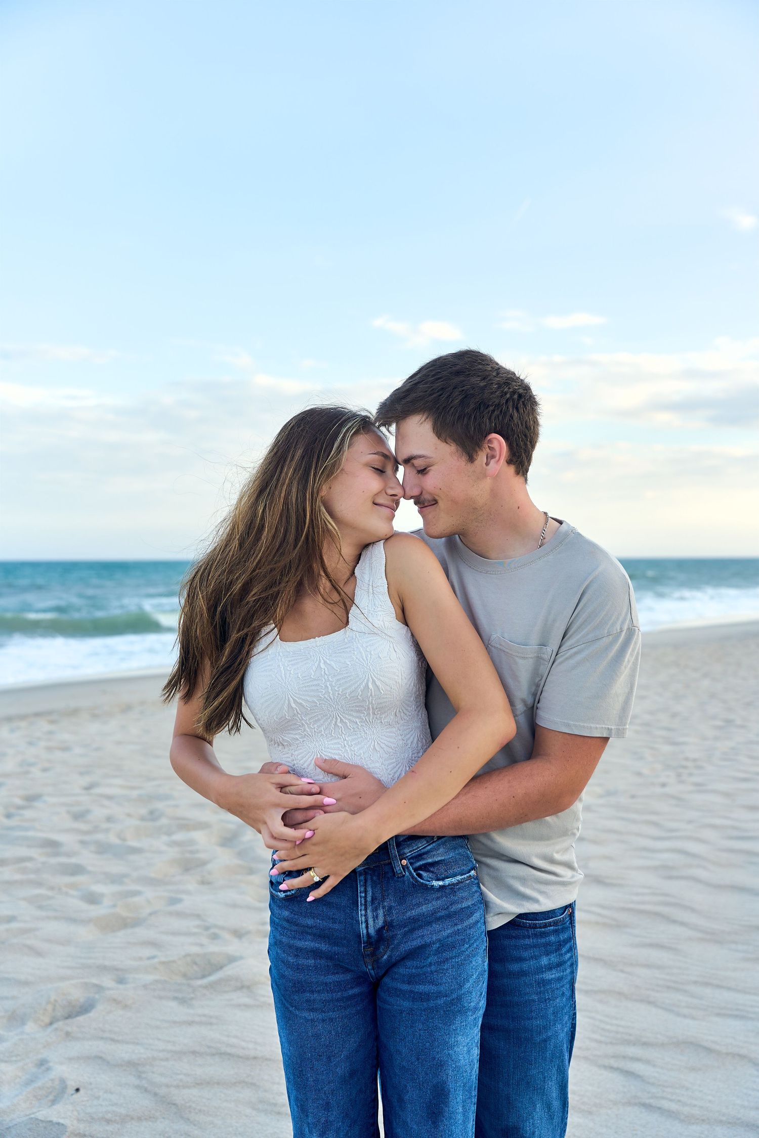 A romantic couple shares an intimate moment together on a sunny beach with ocean waves in the background.