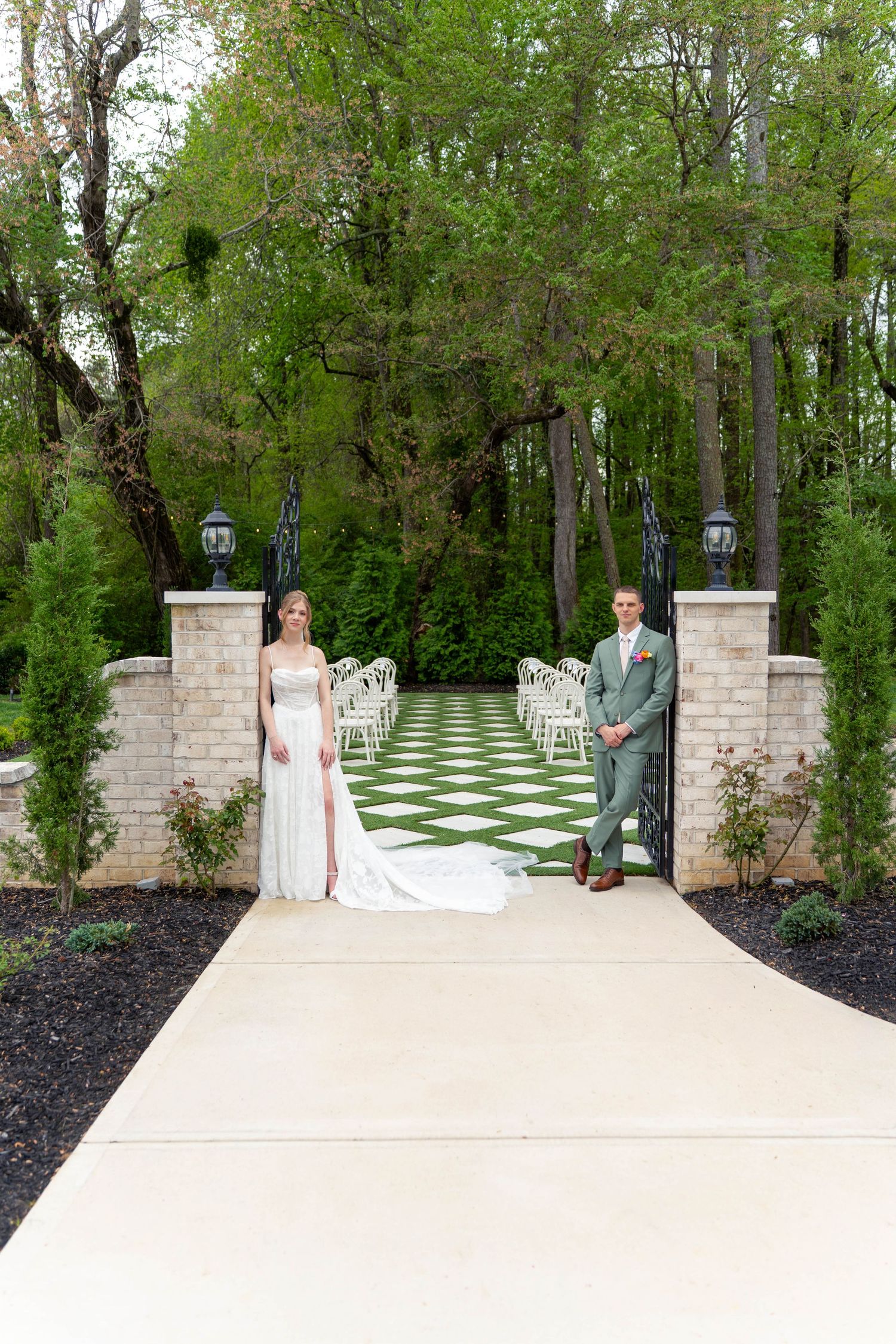 Bride and groom stand at entrance of elegant outdoor wedding ceremony venue with checkered aisle and stone pillars.