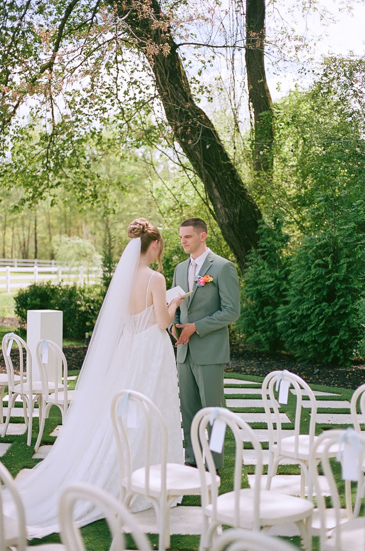 Bride reads vows to groom in sage suit during intimate outdoor garden wedding ceremony.