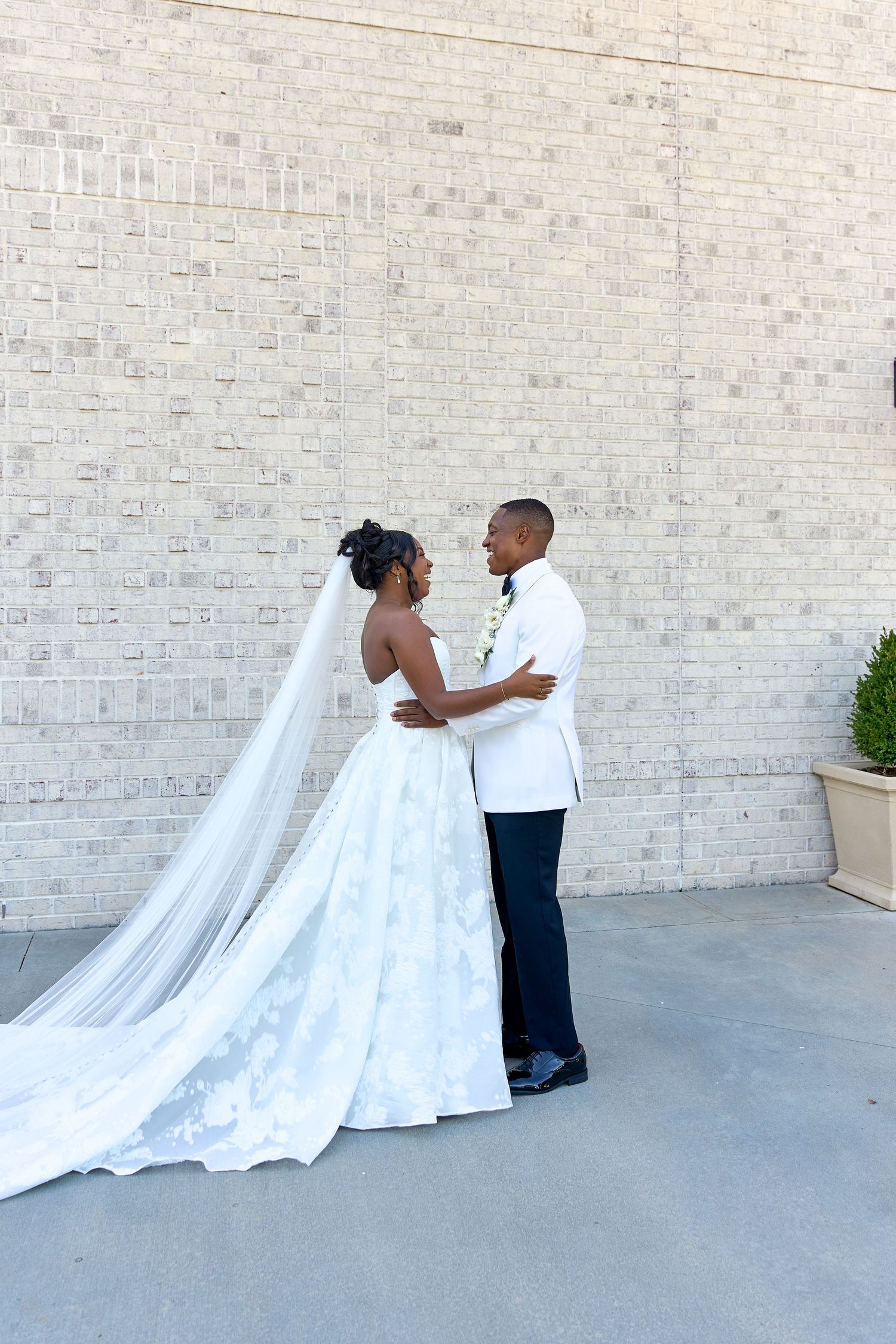 Bride and groom share romantic embrace outdoors, bride wearing lace ballgown with cathedral veil.