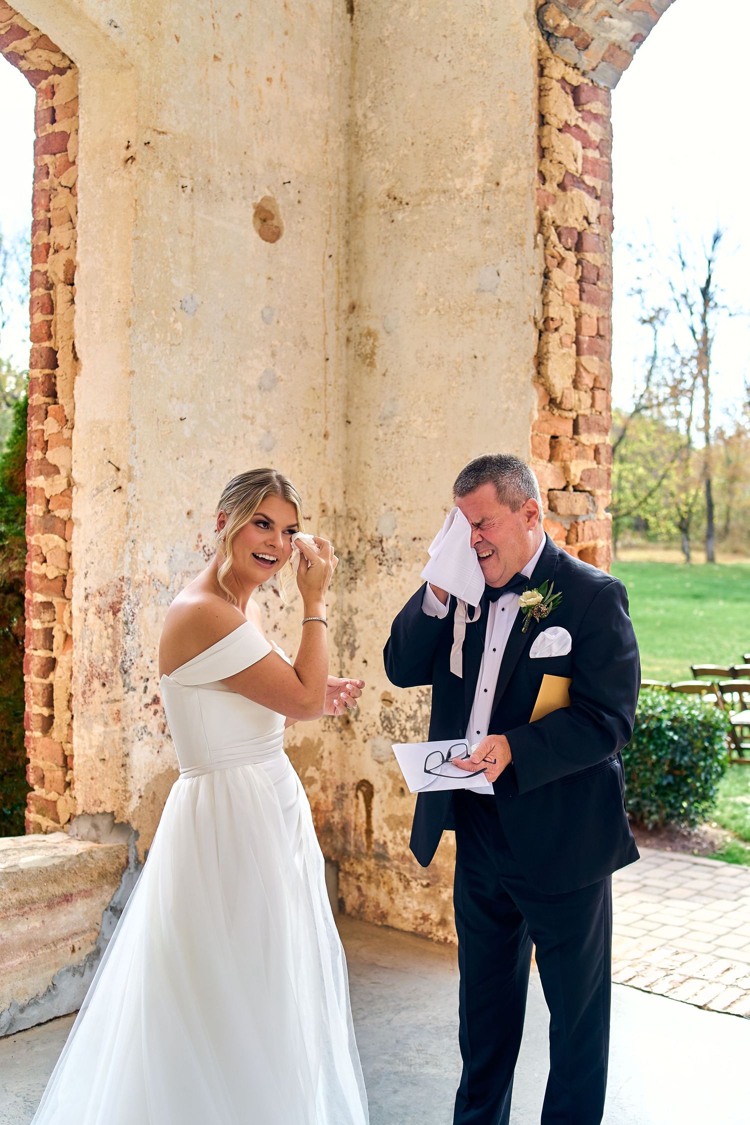 Couple share an emotional first look moment at their wedding under rustic stone archway on outdoor grounds.