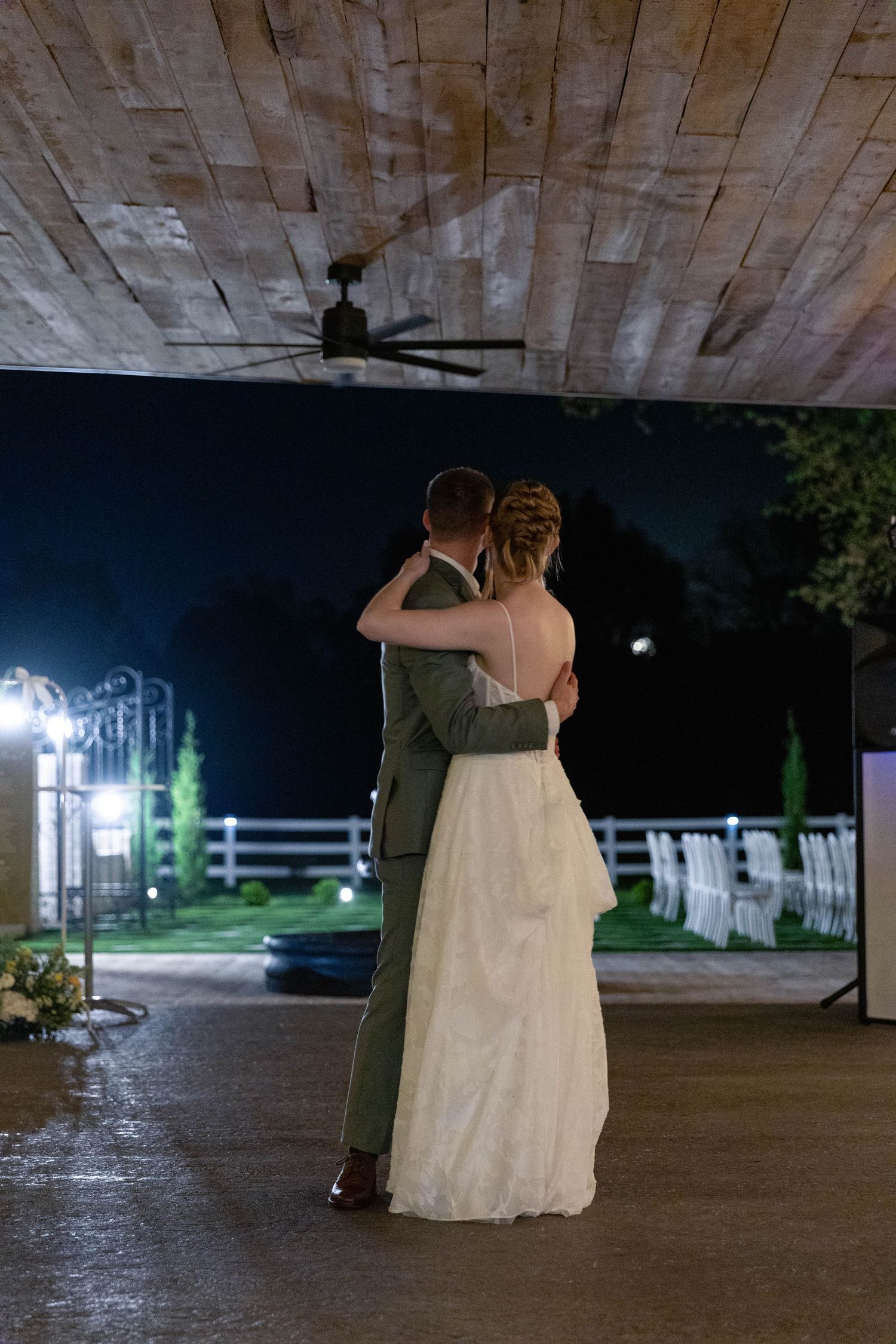 Bride and groom share an intimate first dance under wooden ceiling at outdoor wedding venue at night.