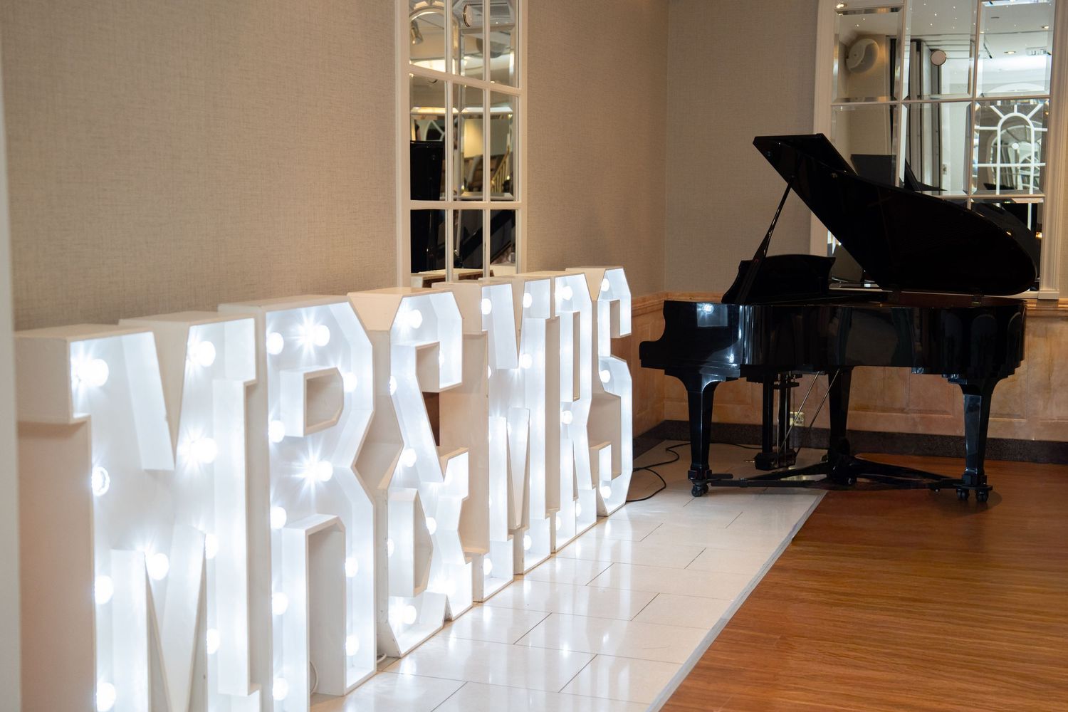 Illuminated MR & MRS marquee letter signs beside a grand black piano on white dance floor at wedding venue.
