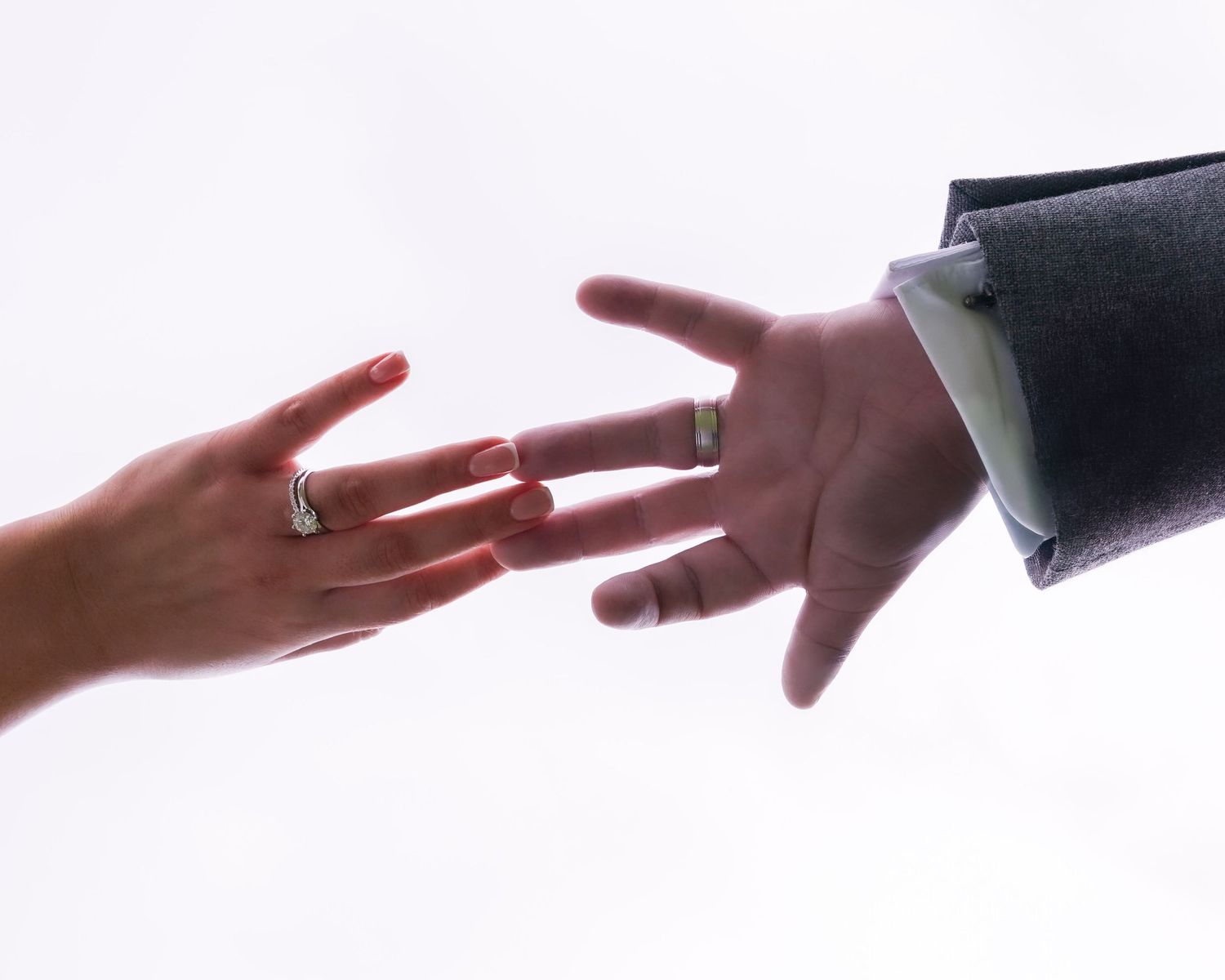 A bride and groom display their wedding rings with outstretched hands.