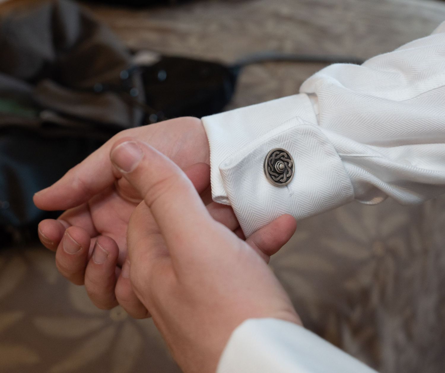 Groom fastening elegant silver cufflinks on white dress shirt sleeve at wedding.
