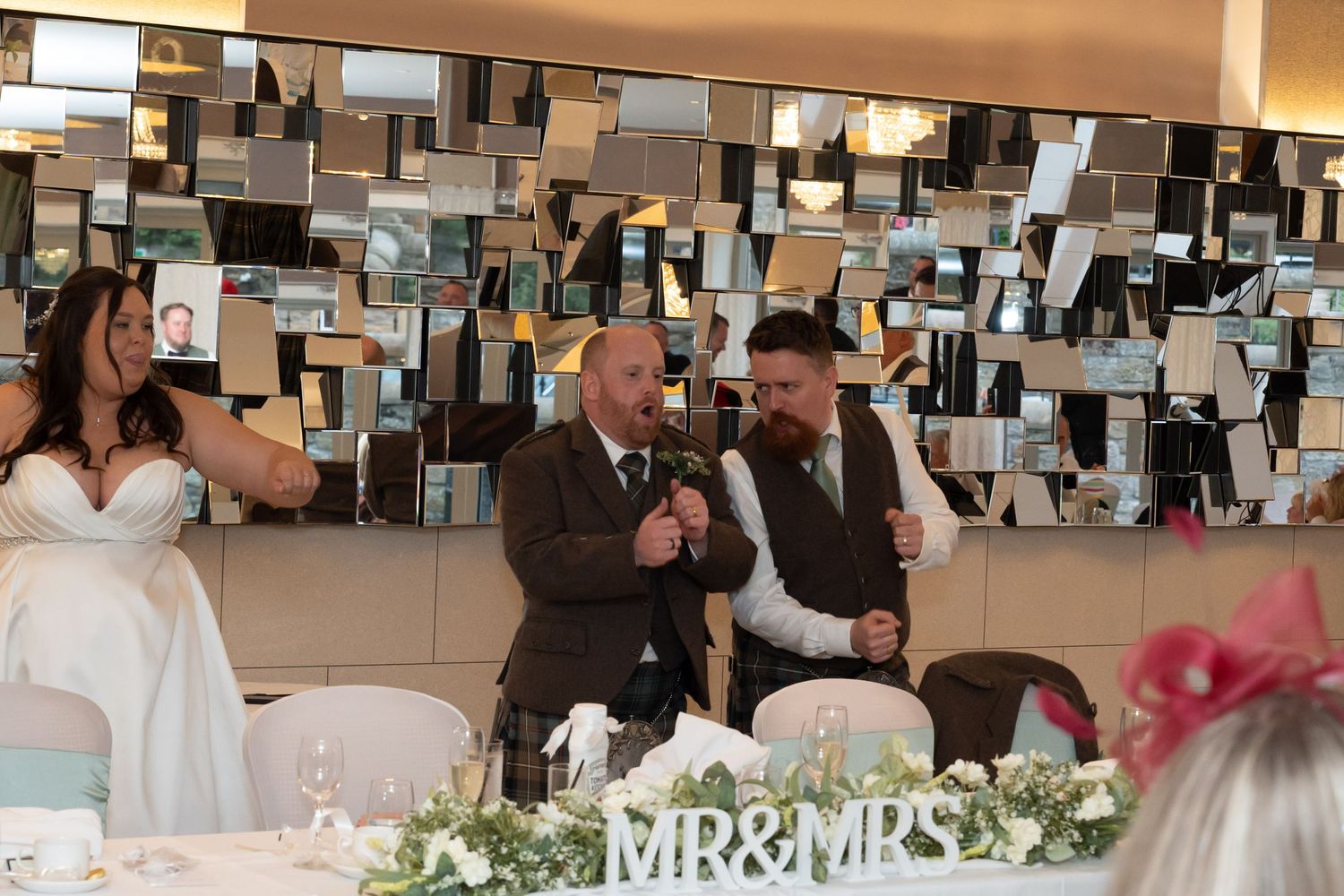 Bride and groom laughing during wedding speeches at decorated MR & MRS table with floral centerpieces.