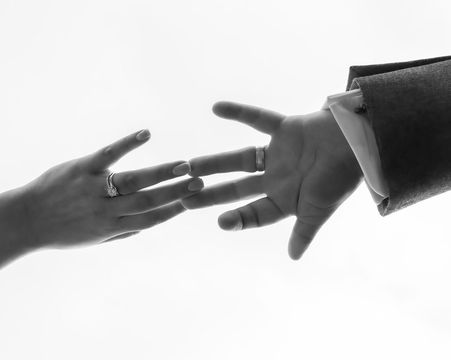 Black and white photo of two hands reaching toward each other, both wearing rings, one holding a book.
