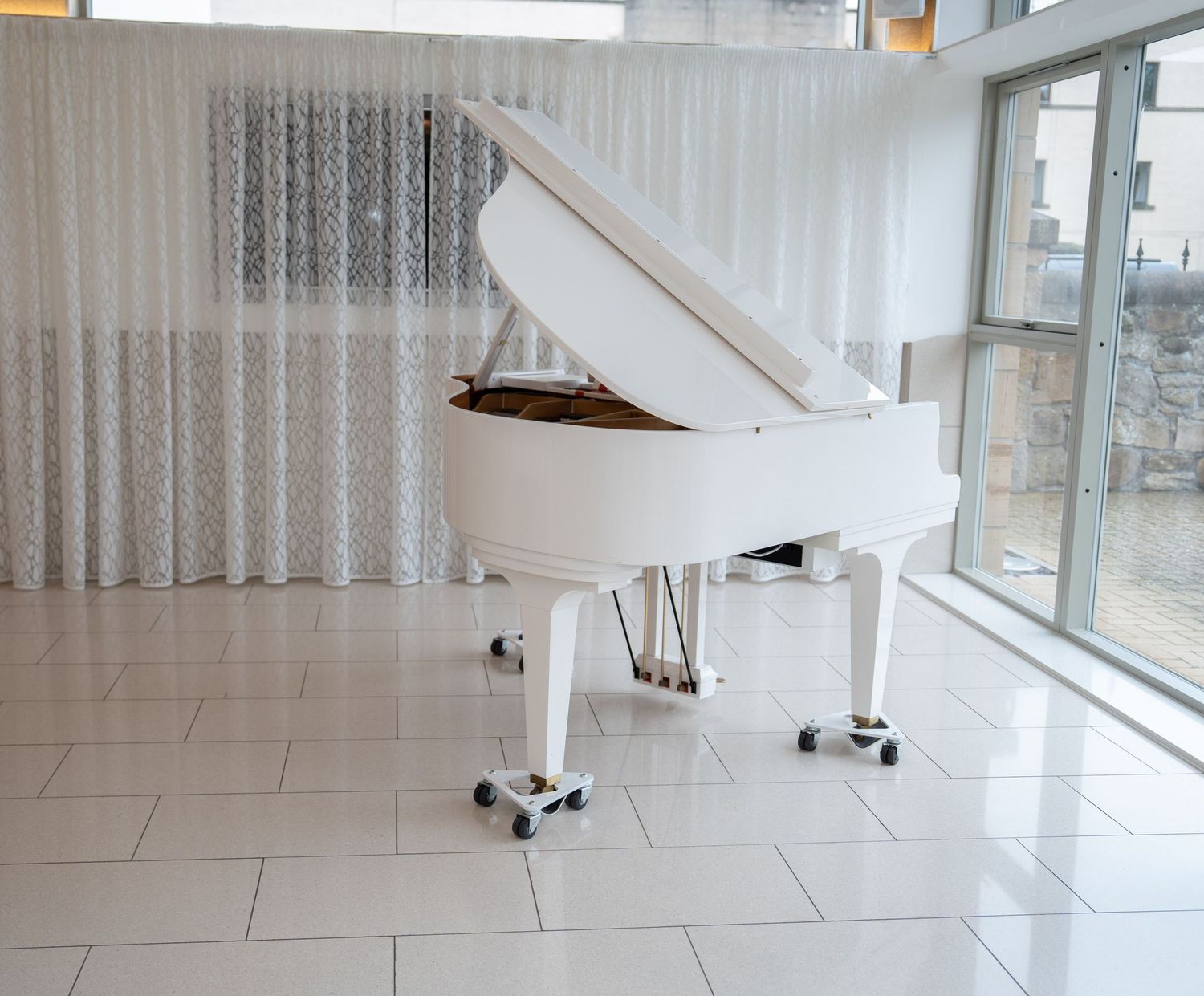 Elegant white grand piano in a bright modern venue with floor-to-ceiling windows.