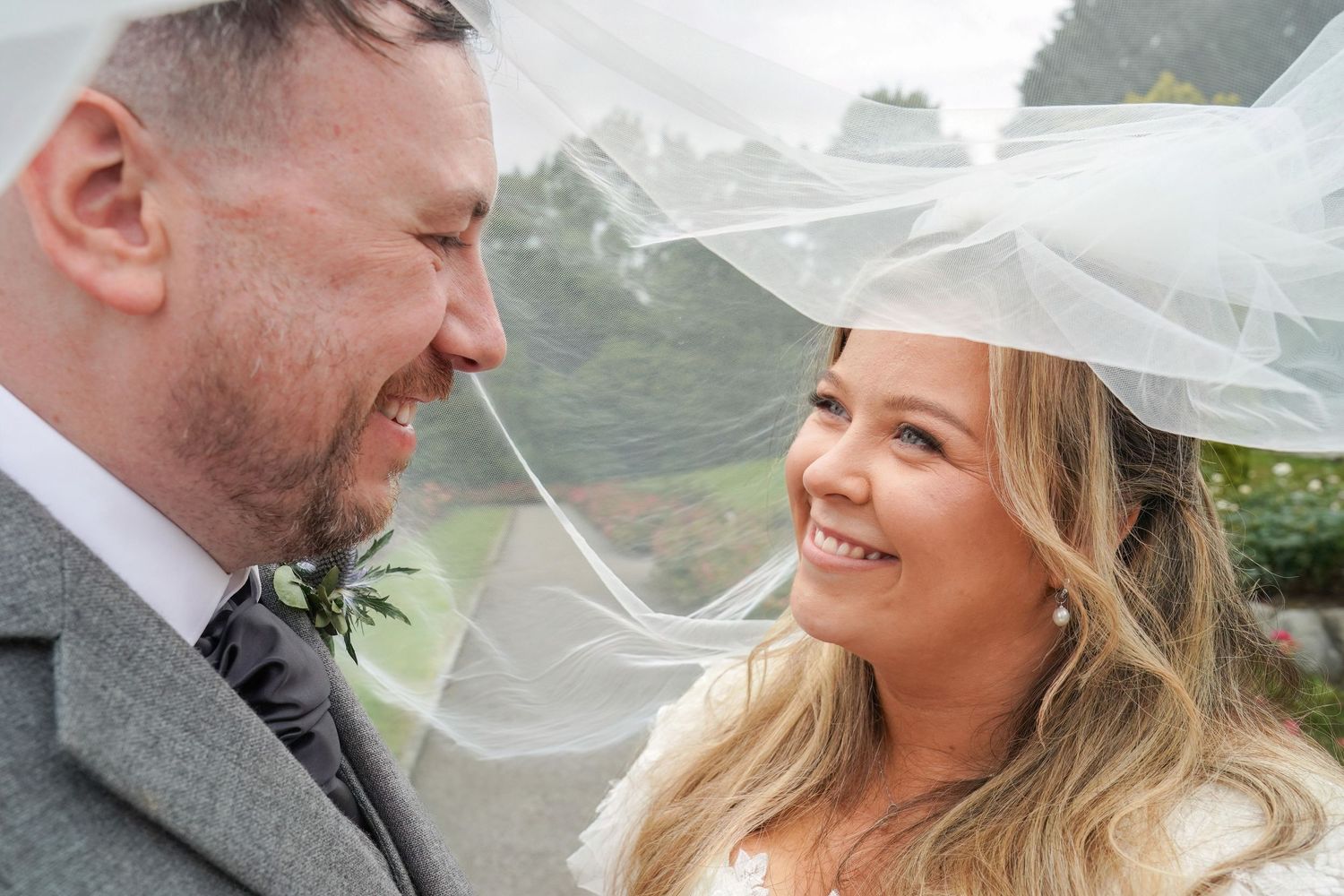Bride and groom smiling under a wedding veil on their rainy outdoor wedding day.