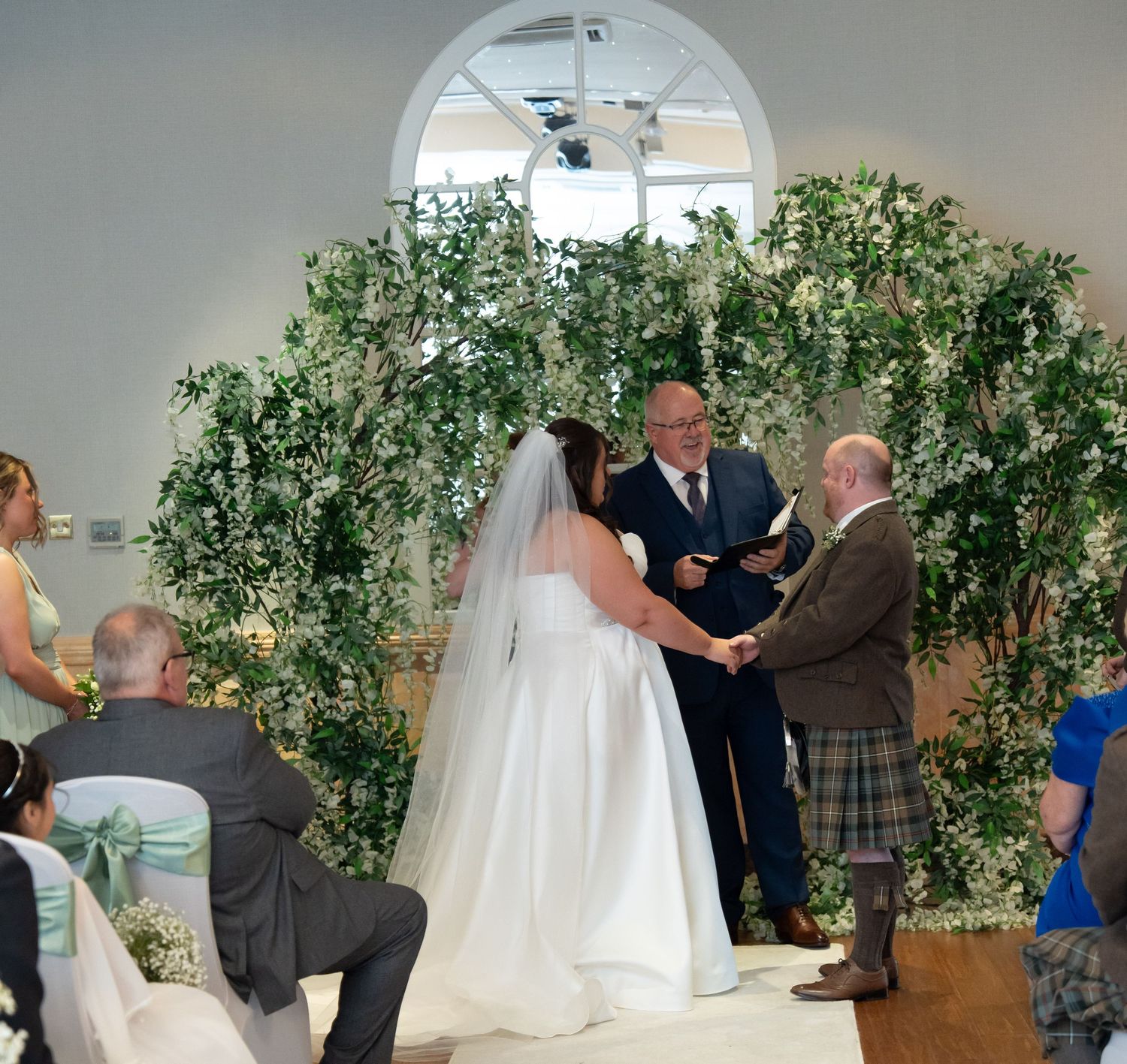 Bride and groom exchanging vows beneath a floral arch at an elegant wedding ceremony.