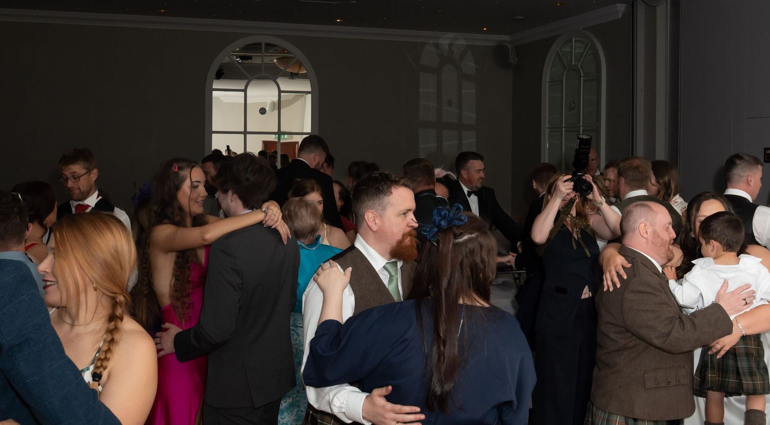 Guests dancing and socializing at a formal evening wedding reception in an elegant dark-walled ballroom.