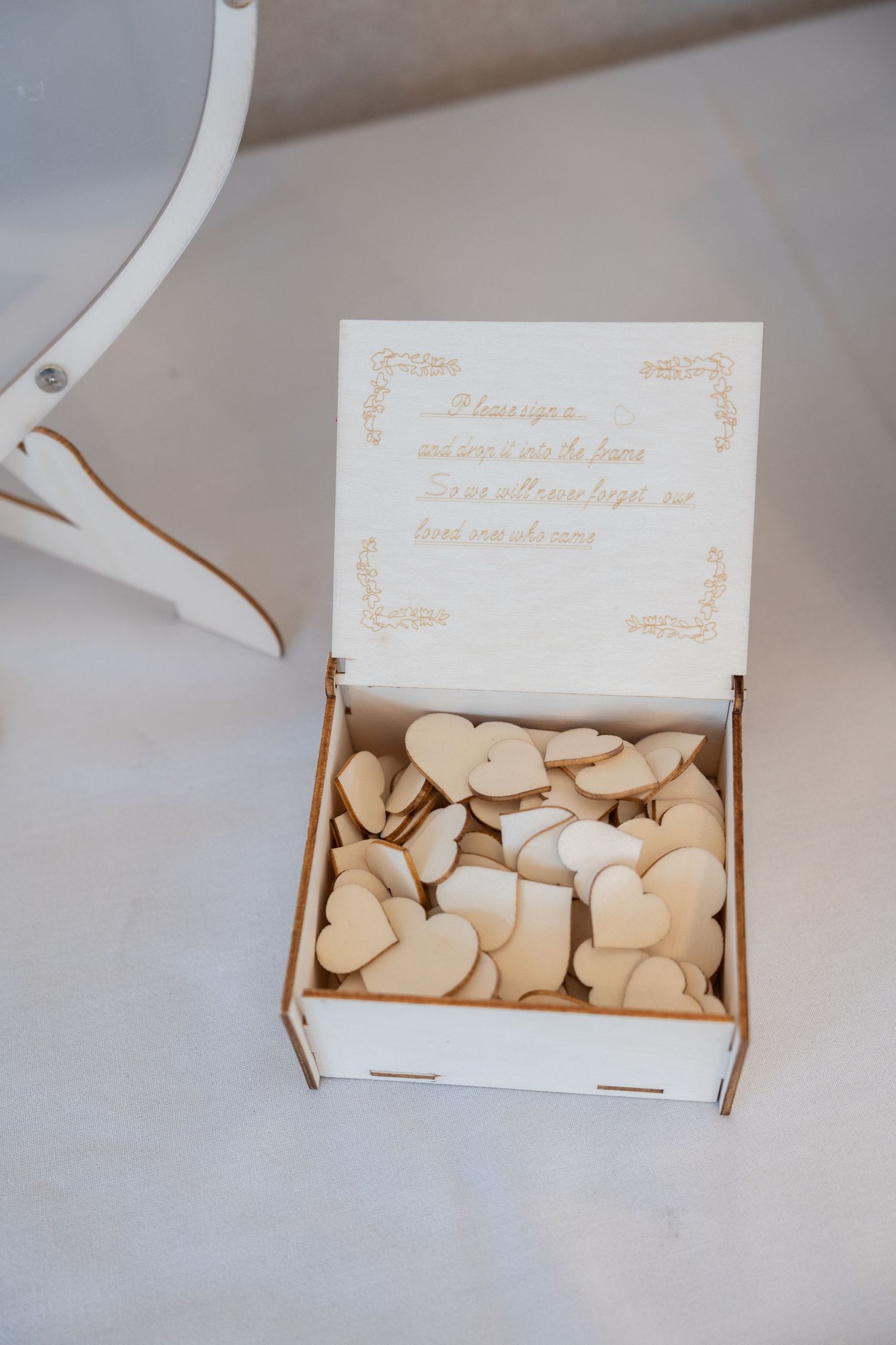 Wooden wedding guest book box filled with small heart-shaped tokens and an engraved message on the lid.