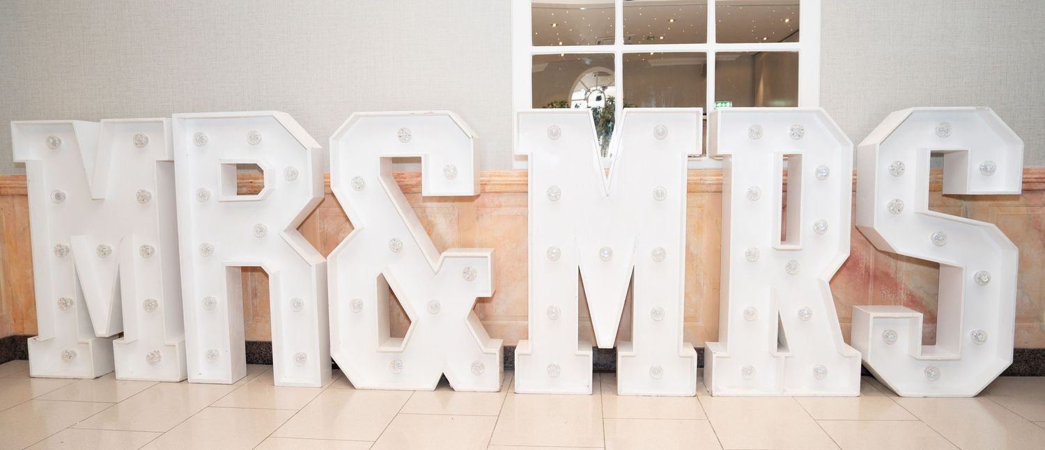 Large illuminated marquee letter signs spelling MR & MRS at a wedding reception venue.