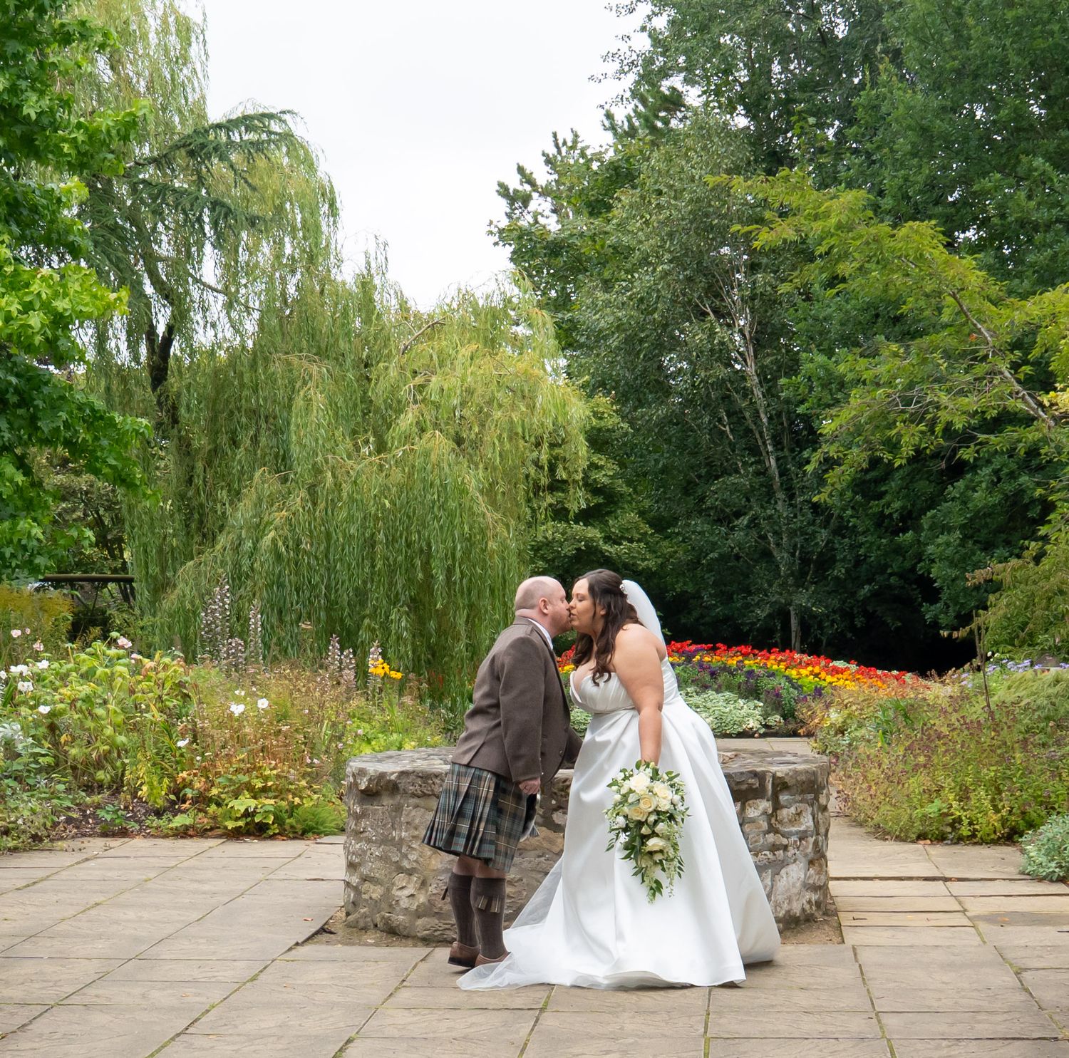 Bride and groom sharing a kiss in lush garden setting during Scottish wedding.