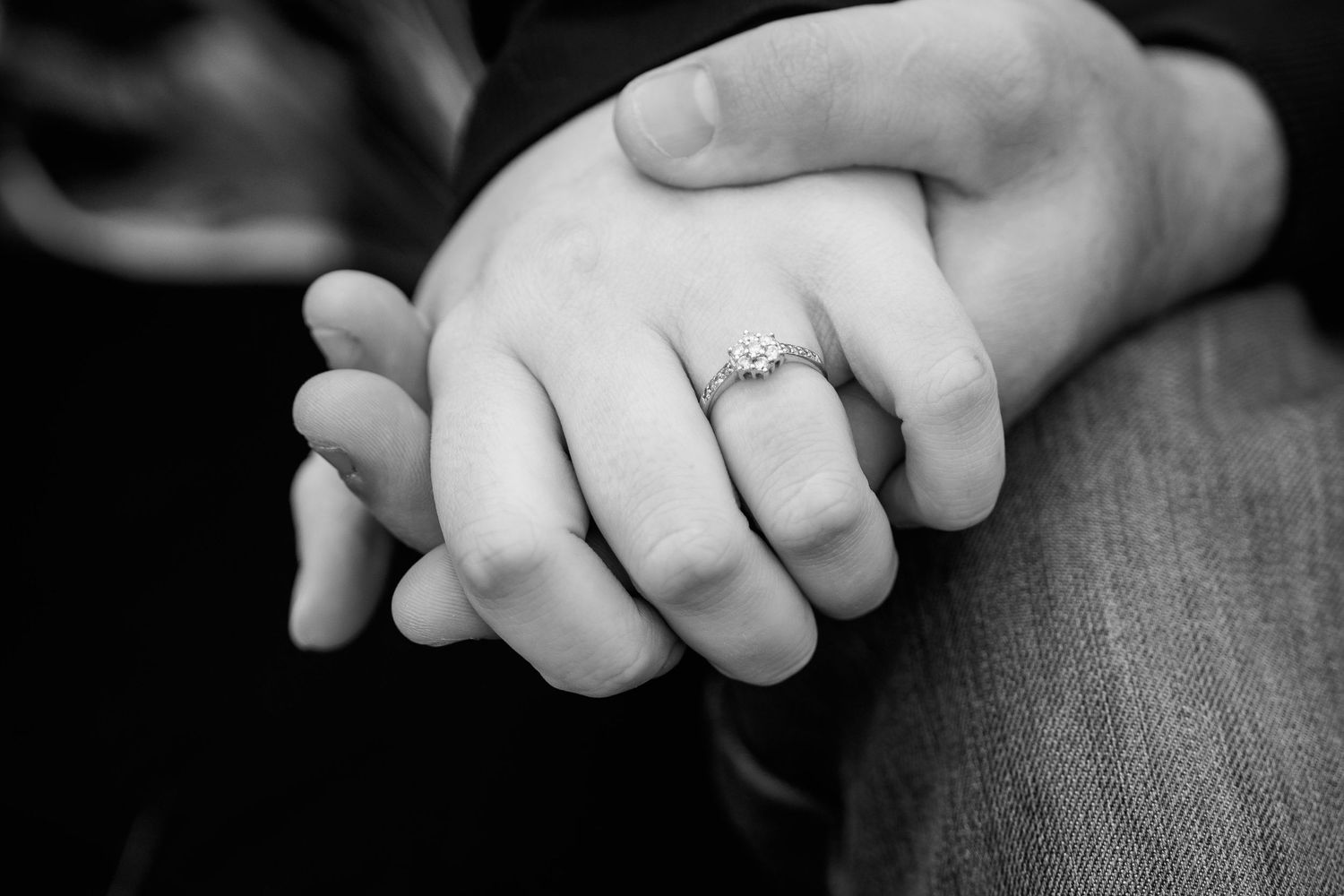 Close-up black and white photo of couple holding hands showing a beautiful diamond engagement ring.