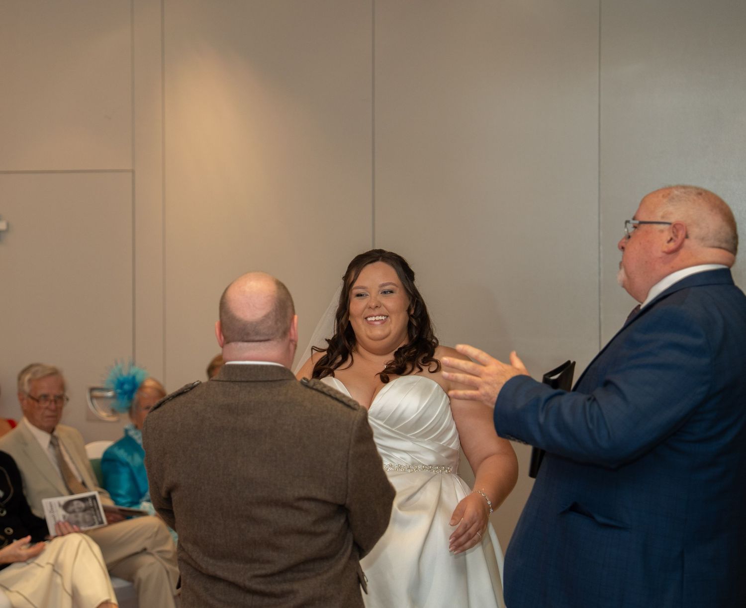Bride in white gown smiling with guests at wedding reception ceremony indoors.