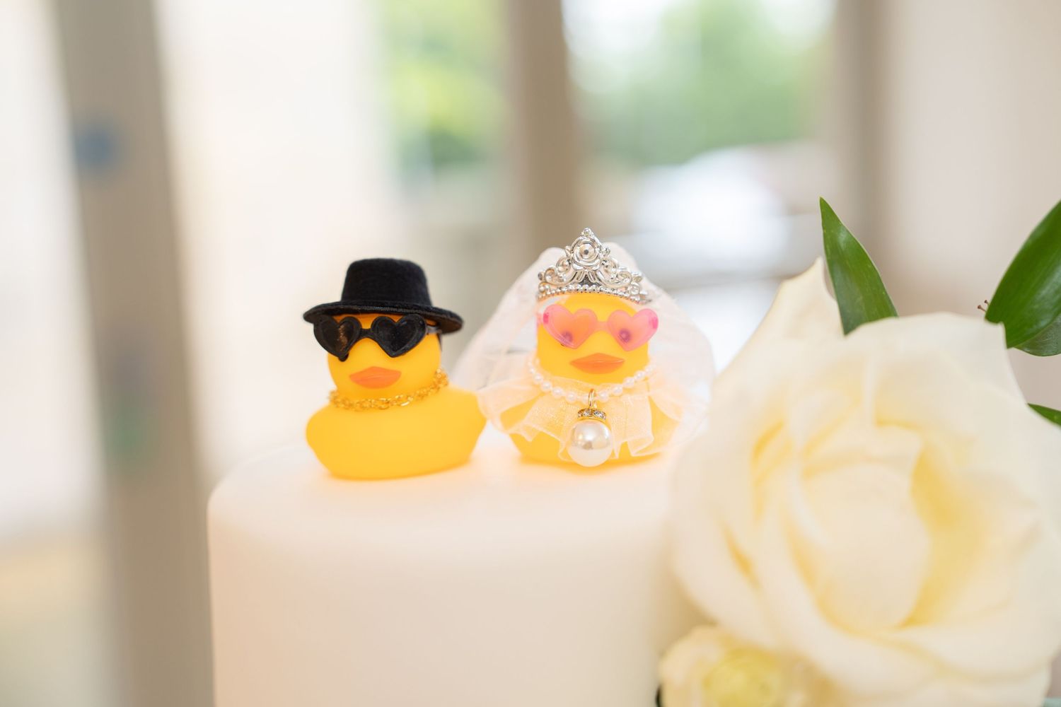 Two yellow rubber duck cake toppers dressed as bride and groom on a white wedding cake.
