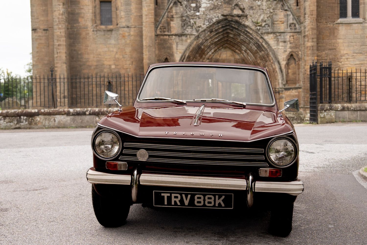 Vintage dark red classic car with license plate TRV 88K parked on cobblestones near a historic stone building.