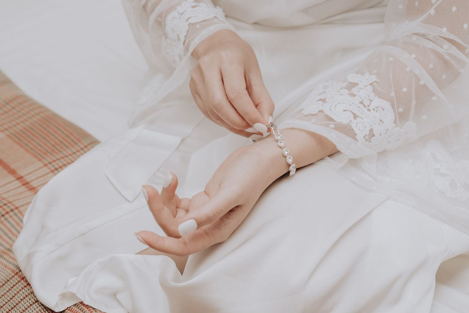 Bride in white lace dress fastening a pearl bracelet on her wrist on her wedding day.