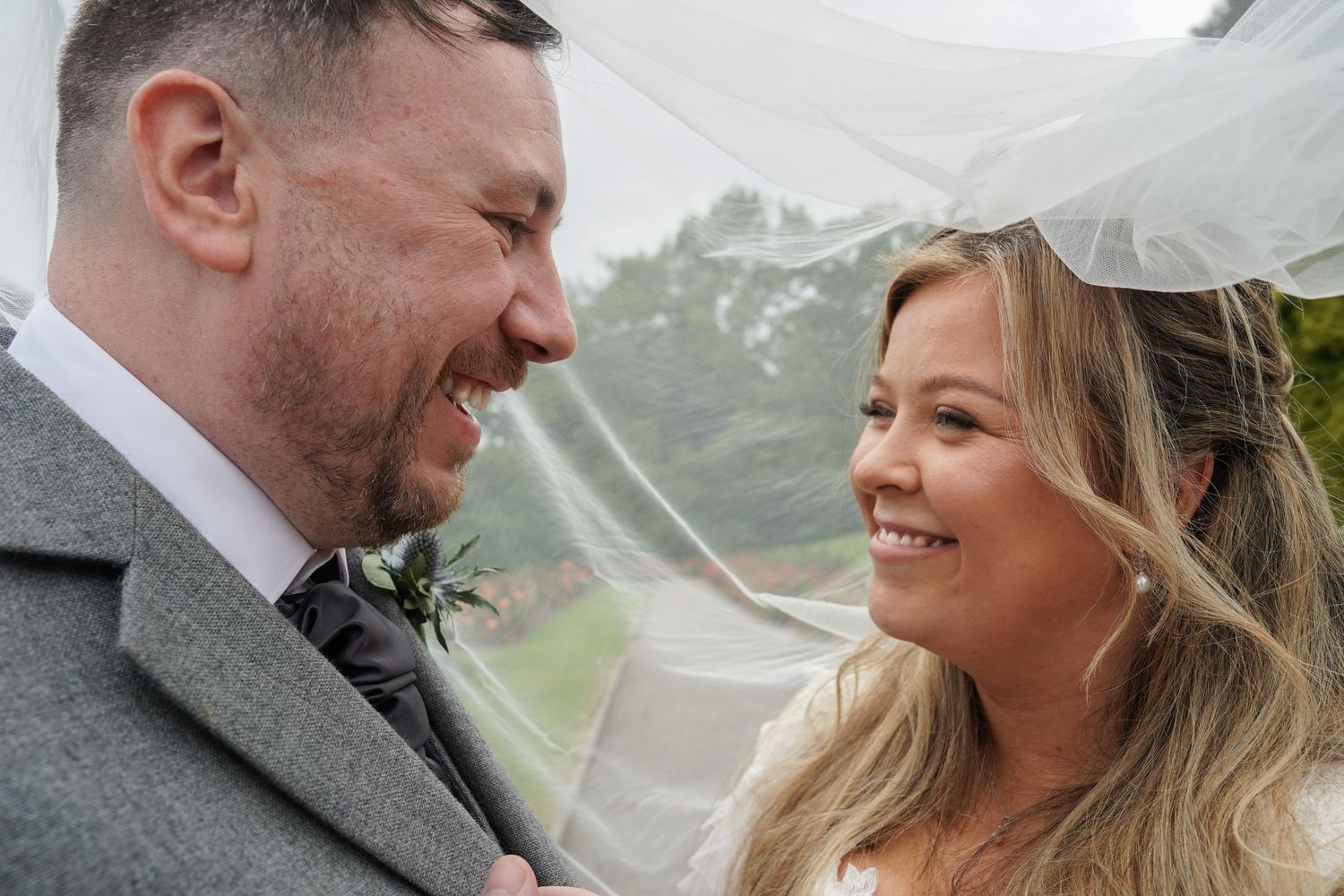 Laughing bride and groom sharing an intimate moment under a veil in the rain on their wedding day.