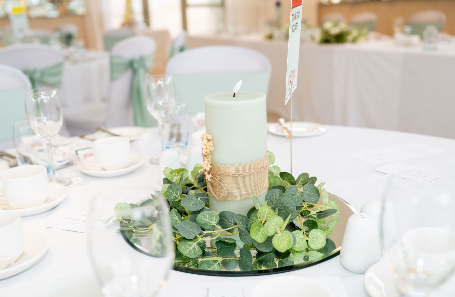 Elegant wedding table centerpiece with a mint pillar candle, gold twine, and fresh eucalyptus on a mirrored base.