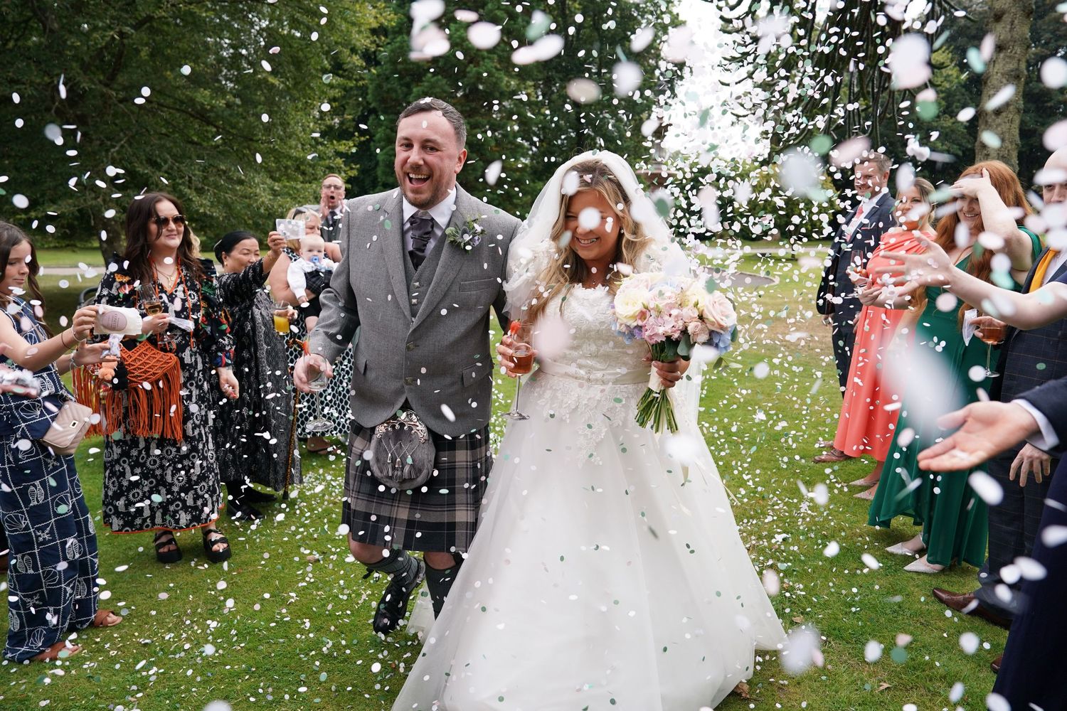 Bride and groom laugh joyfully as confetti fills the air during outdoor wedding celebration.