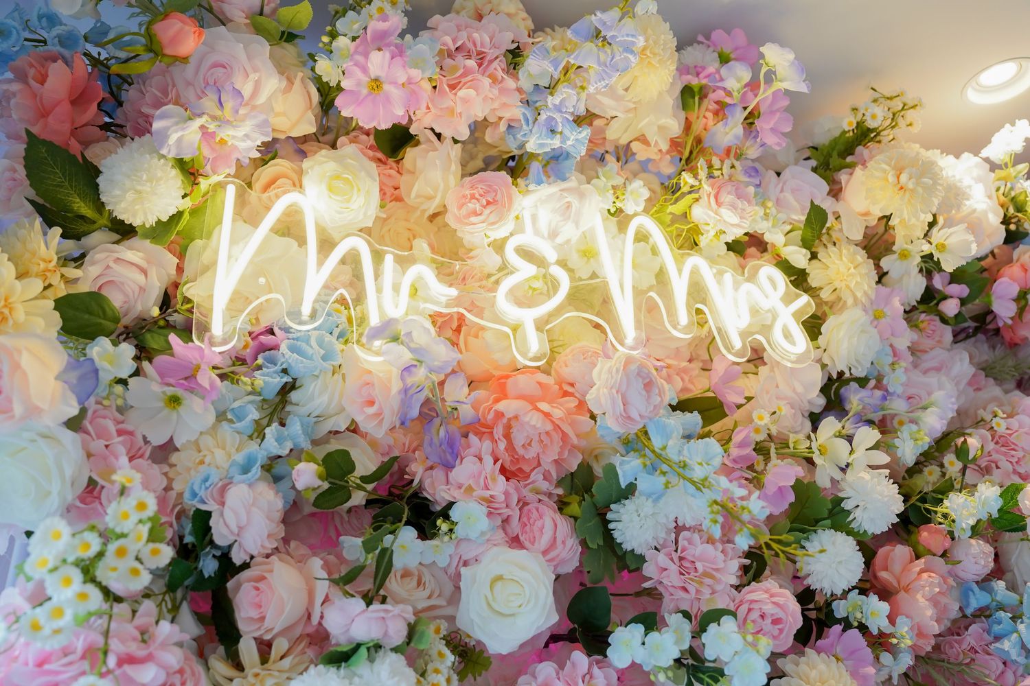 Romantic Mr and Mrs neon sign surrounded by pastel pink and white floral wedding wall backdrop.
