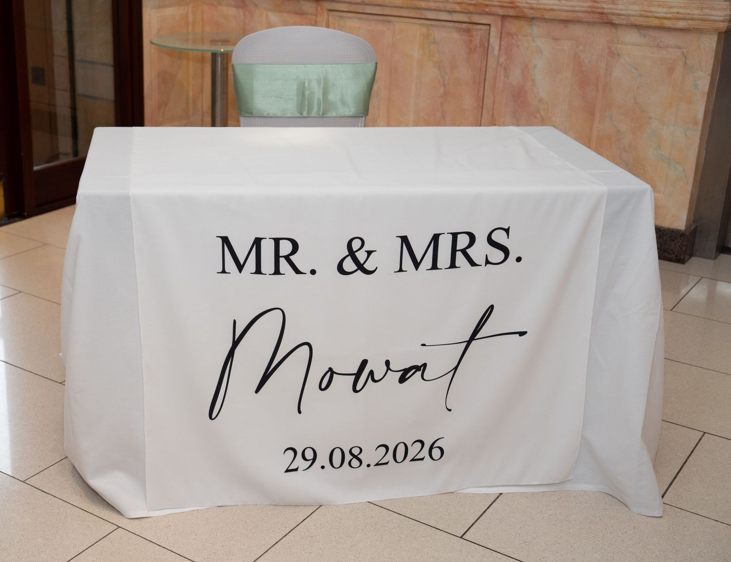 White wedding table cover printed with Mr. & Mrs. Mowat and date 29.08.2026 displayed at a wedding reception.