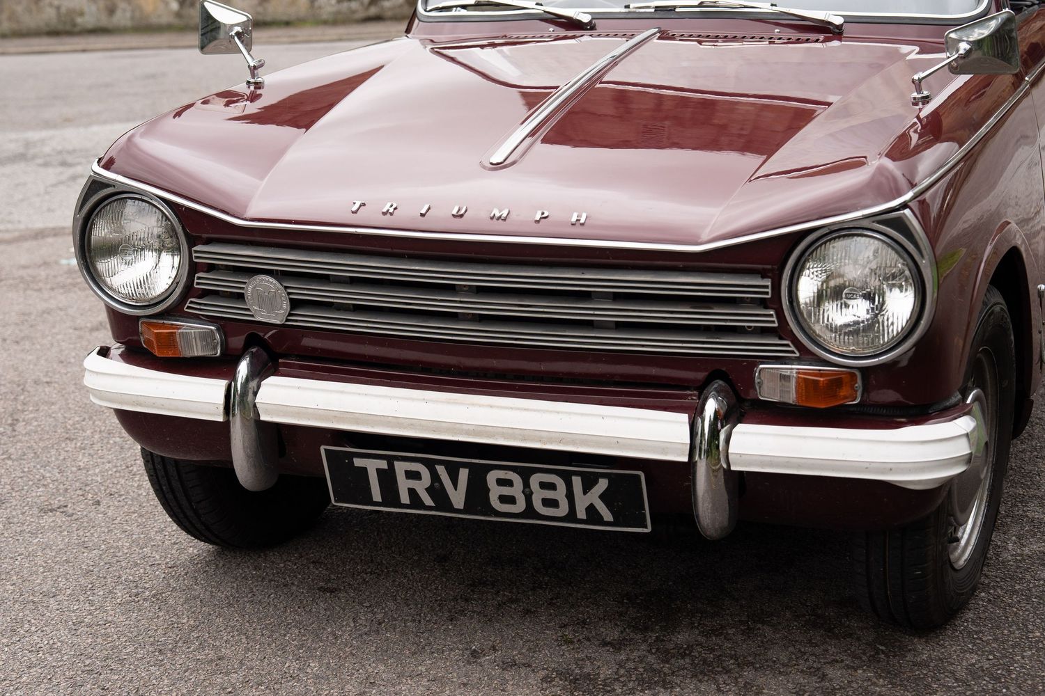 Vintage Triumph TR6 classic car in burgundy red with chrome bumper bar at a wedding venue.