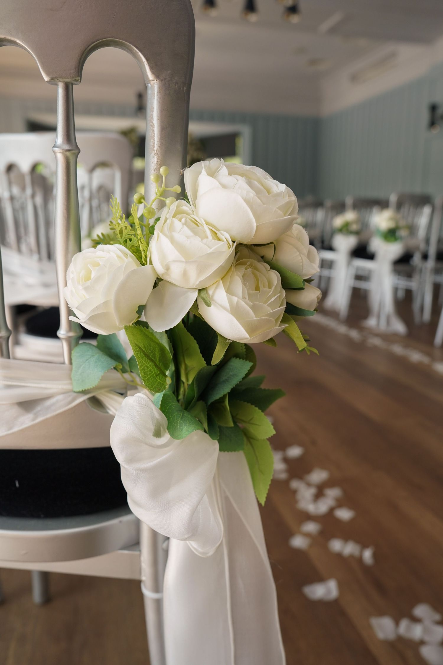 Elegant white rose bouquet tied with white ribbon decorating a silver chair at a wedding venue.