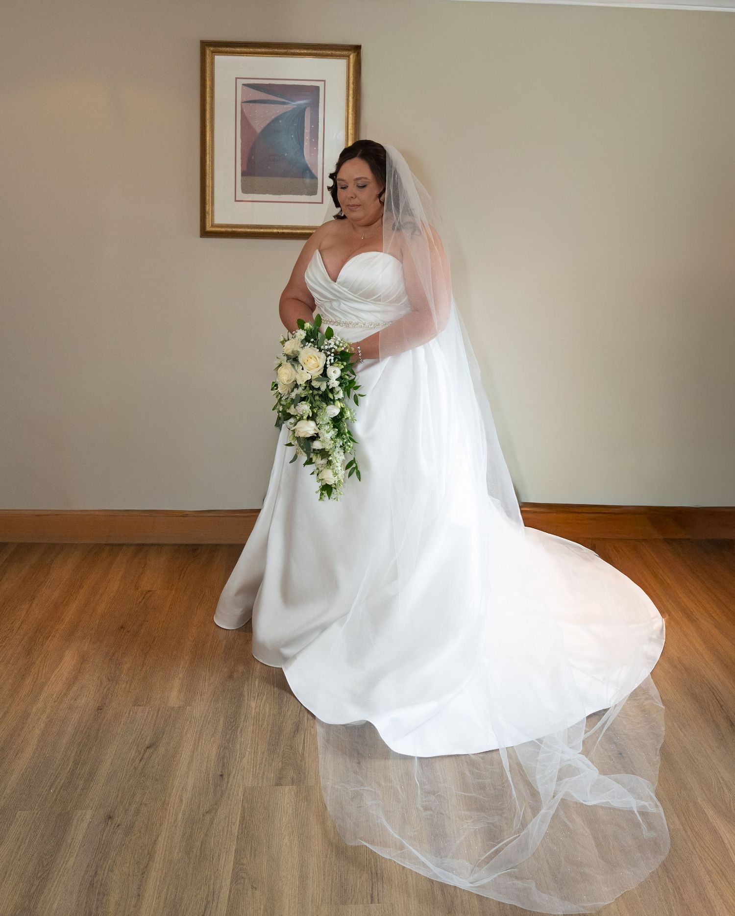 Bride in strapless white ball gown with long veil holding a cascading bouquet of white roses.