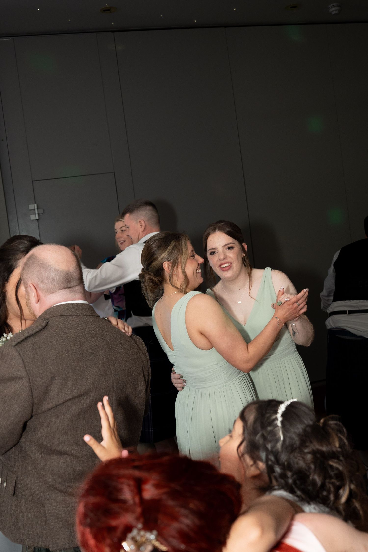 Two bridesmaids in mint green dresses dancing together joyfully at a lively wedding reception.