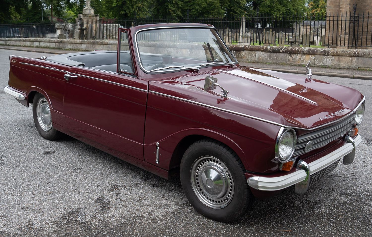 Classic dark red Triumph Herald convertible vintage car parked outdoors in pristine restored condition.