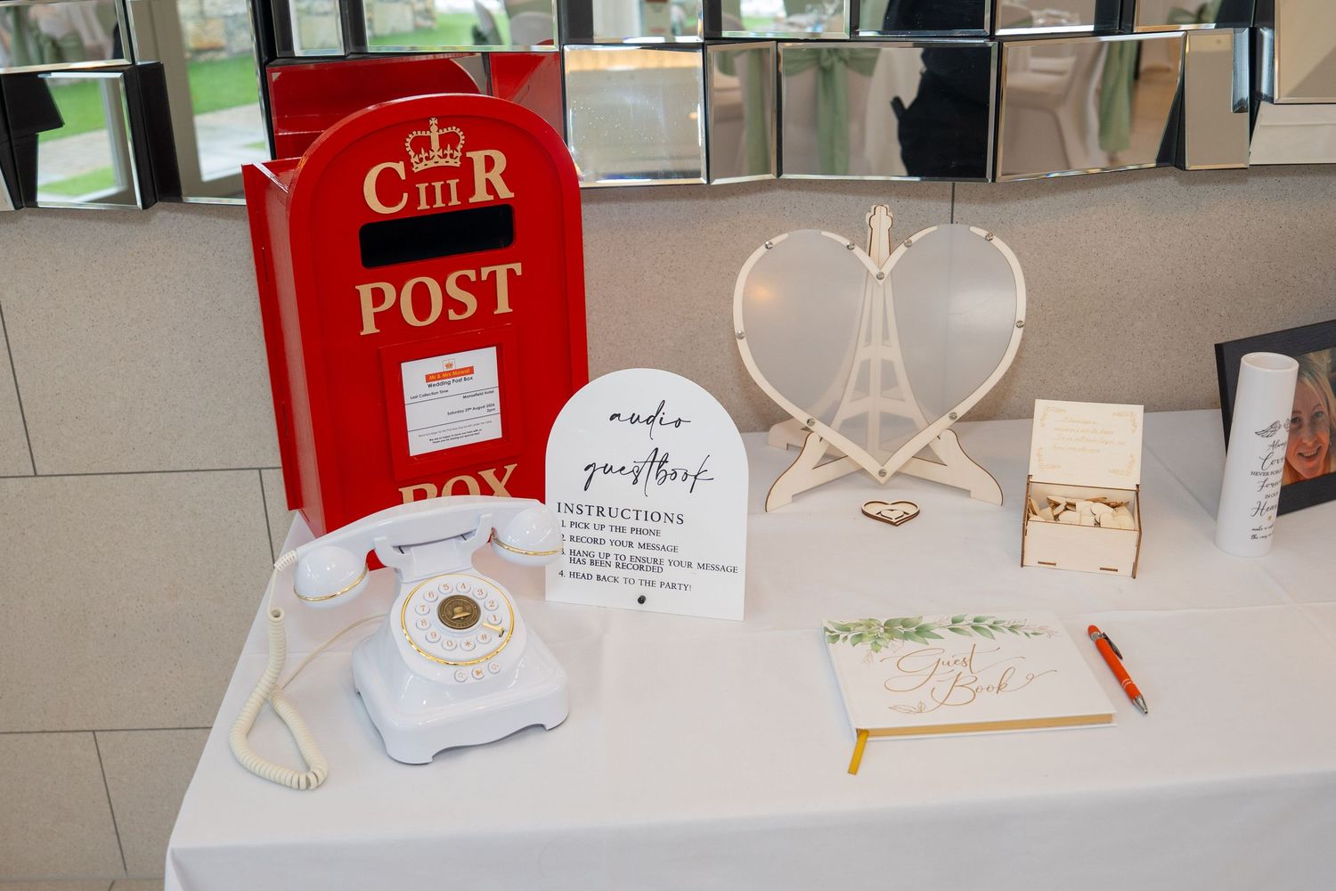Wedding guest book table with red Royal Mail post box, white vintage phone, heart frame, and audio guestbook sign.