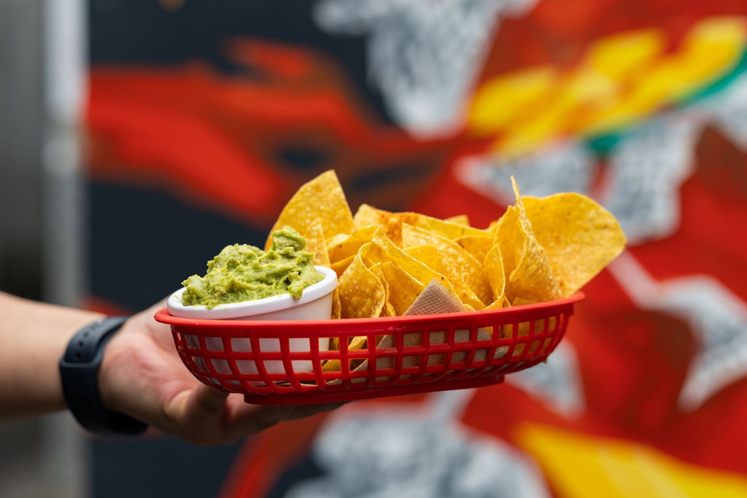 Claire House Photograph business photograph of a hand holding Cadera nachos and guacamole in front of a colourful mural.