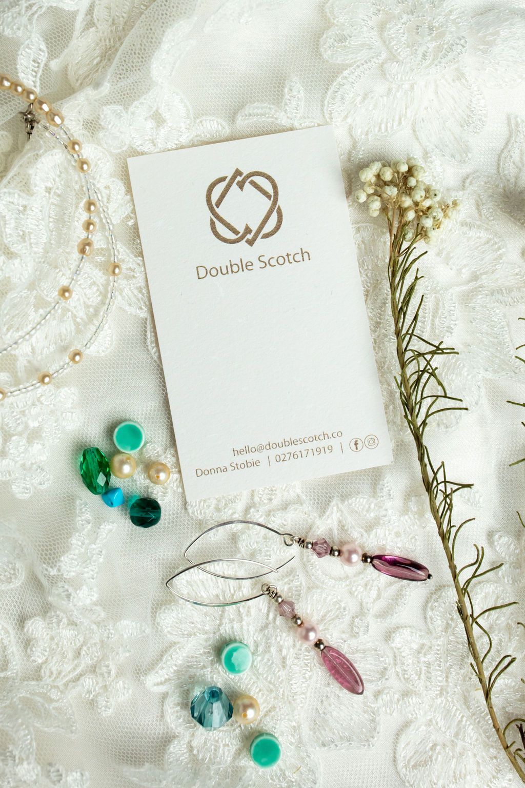 Claire House Photography product photograph of ethically made earrings and necklace with business card on lace background.