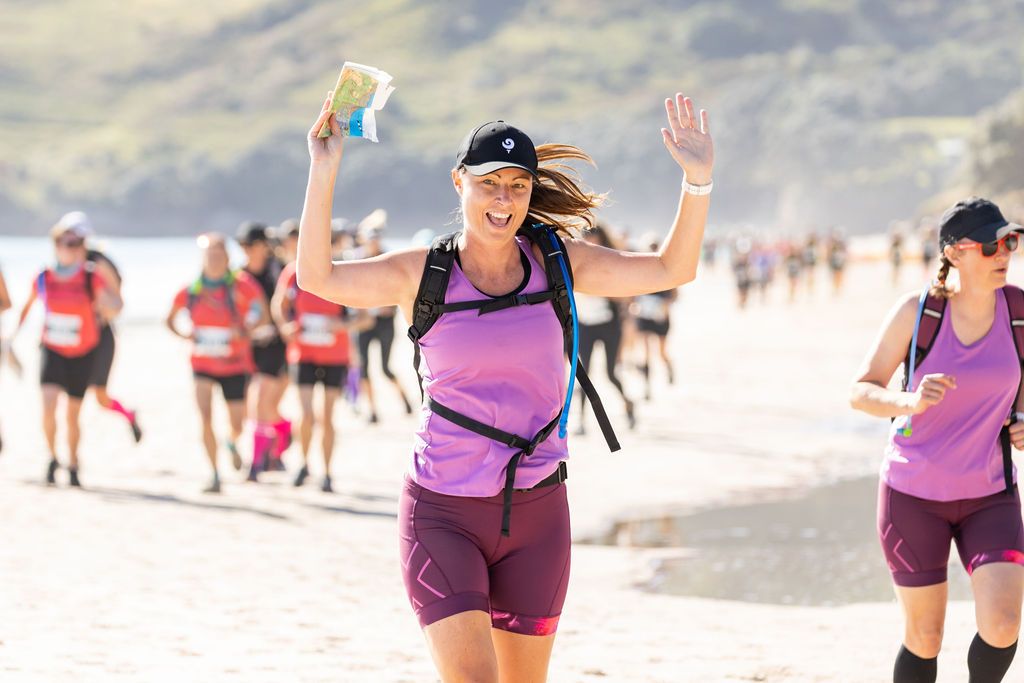 Claire House Photography sports event photograph of a woman running holding an adventure race map and smiling.