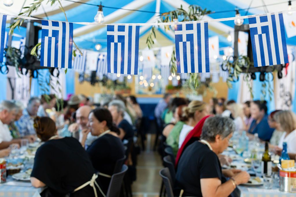 Claire House Photography event photograph of a Flavours of Plenty food event showing Greek flags and guests eating at a long table.